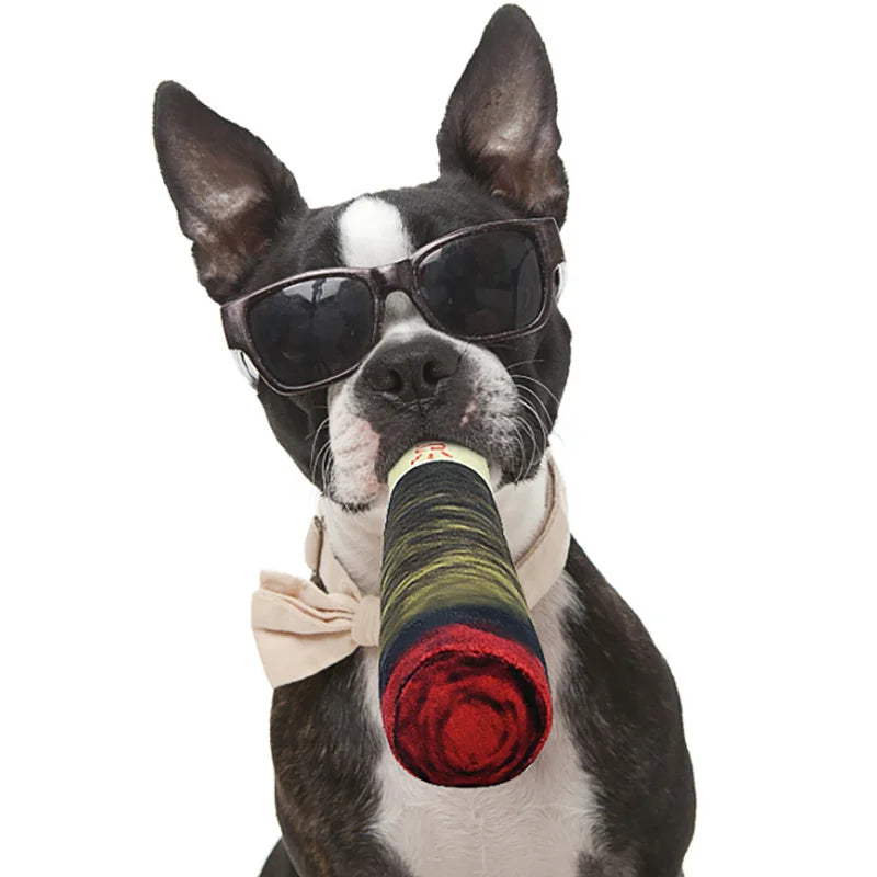 A stylish Boston Terrier wearing sunglasses and a bow tie holds a toy bottle in its mouth, exuding playful confidence.