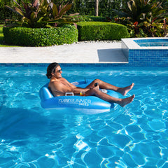 A person relaxes on PoolCandy Tube Runner Pro 2.0 float in a clear blue pool, enjoying a sunny day surrounded by lush greenery.