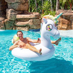 A man lounges on a PoolCandy motorized unicorn pool tube float in a clear blue pool. A waterfall flows in the background