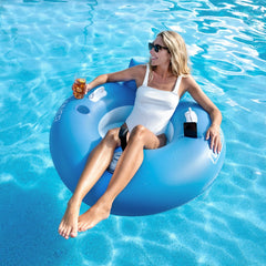 A woman relaxes on a Tube Runner Pro 2.0 float in a clear blue pool, enjoying a sunny day surrounded by lush greenery.